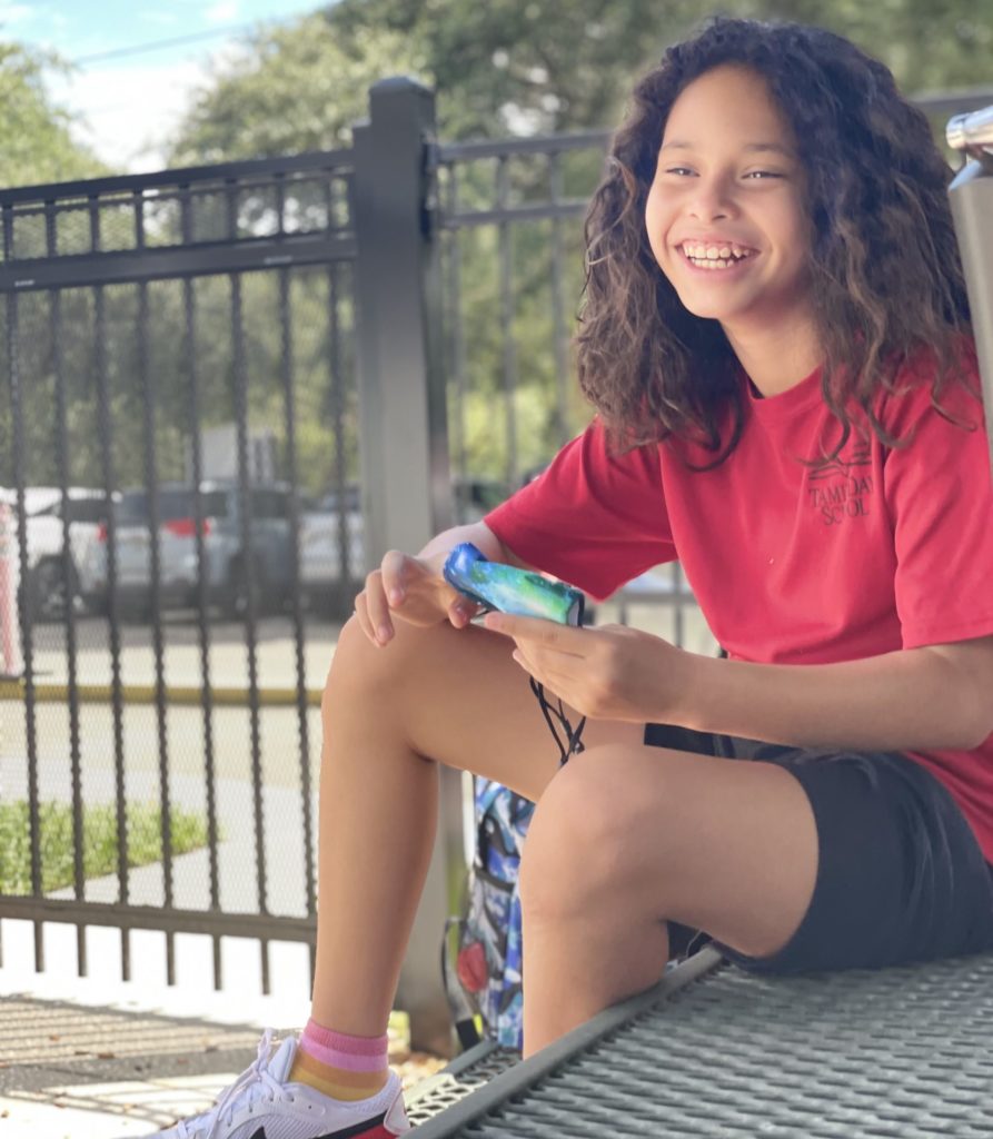 Female Student sits outside and smiles during recess at Tampa Day School