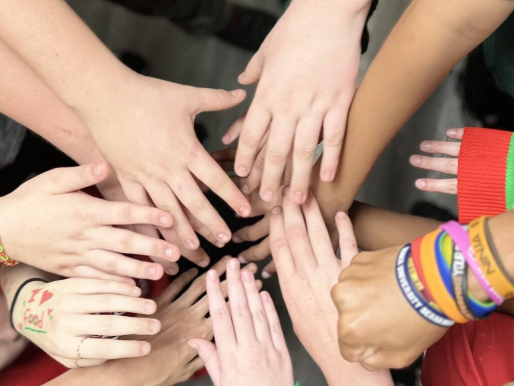 Teens put hands in center to show teamwork before an improv show at Tampa Day School.